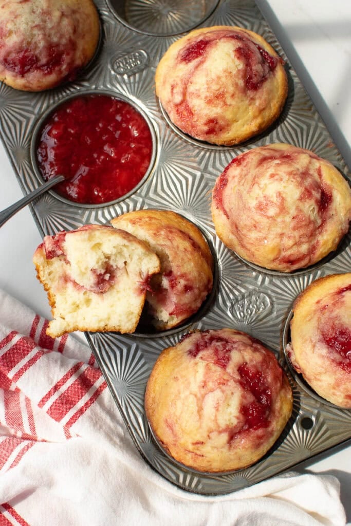 A pan of strawberry muffins with one muffin tin filled with strawberry sauce.