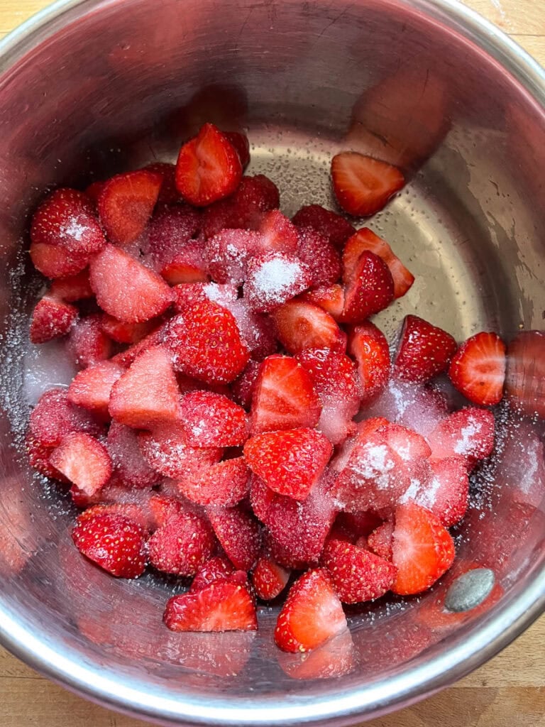 A sauce pan with cut fresh strawberries and sugar before cooking.