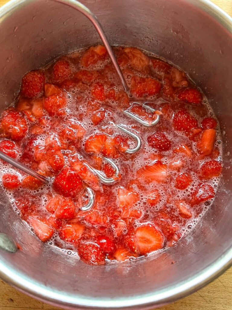 A sauce pan of strawberry sauce cooking on the stovetop.