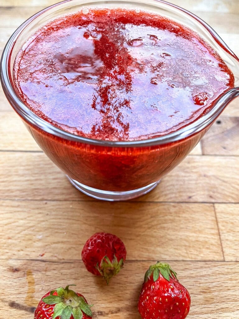 Freshly made strawberry sauce in a small glass pitcher.