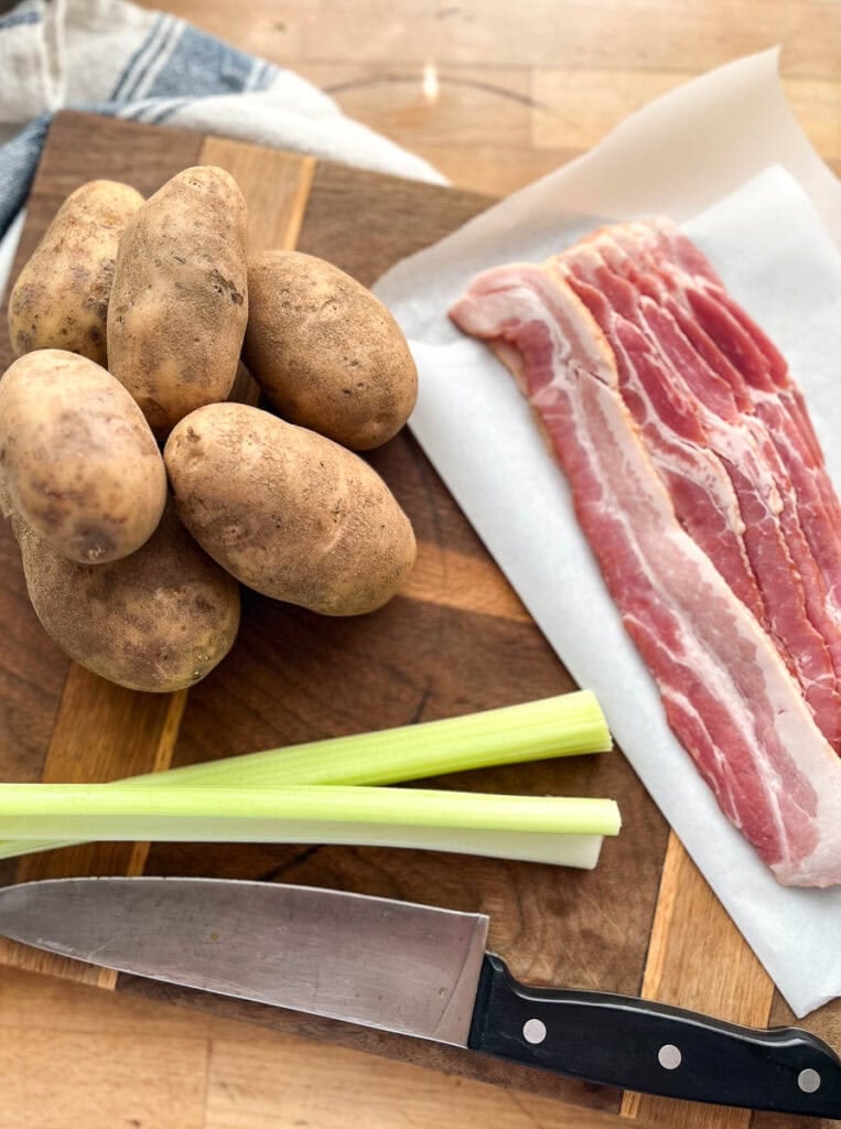 Russet potatoes, thick cut bacon on parchment paper and 2 stocks of celery on a cutting board.