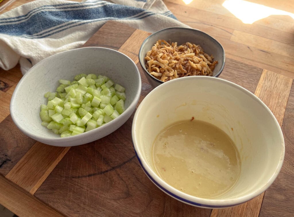 Creamy dressing, chopped celery and crispy French fried onions in small bowls on a cutting board.