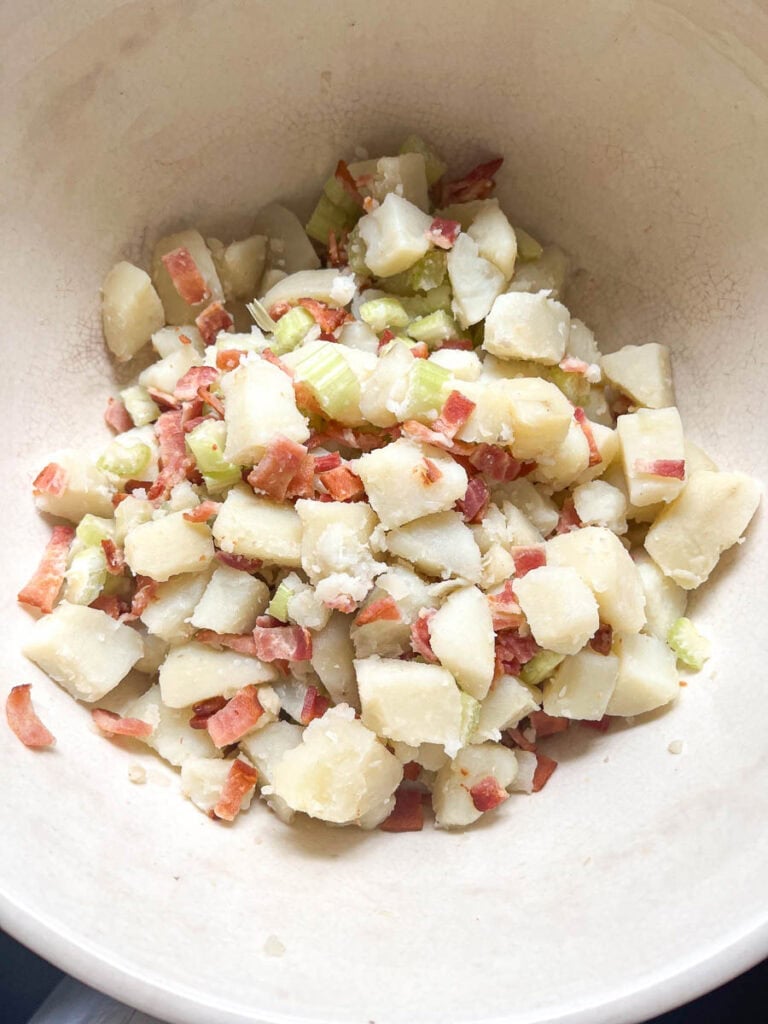 Cooked potato cubes I a bowl with crispy bacon pieces and chopped celery.
