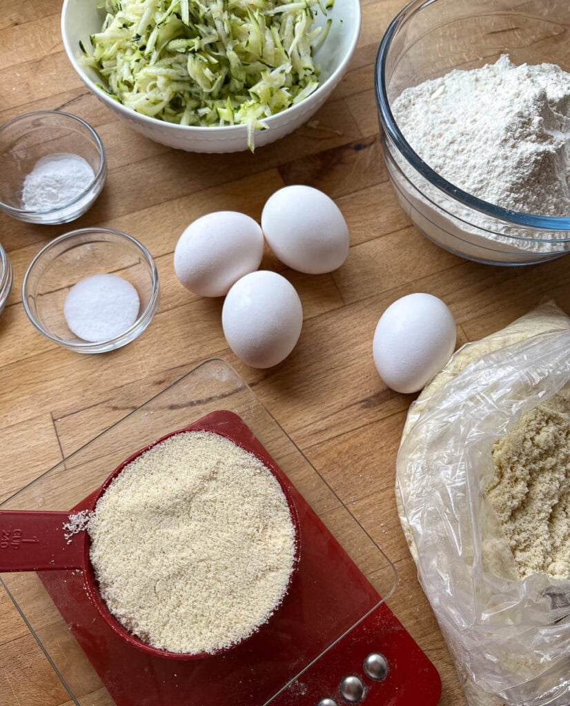 Ingredients to make almond zucchini bundt cake including eggs, almond flour, freshly grated zucchini, and sugar.