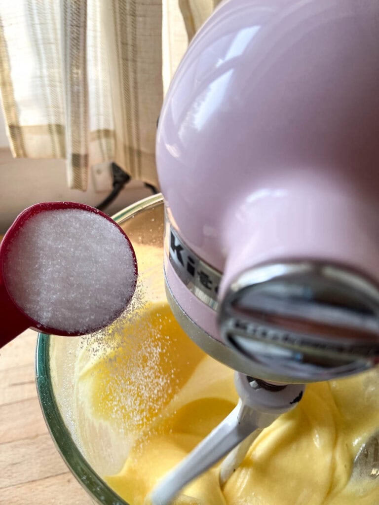 Sugar being gradually added to beaten eggs in a slow steady stream while mixer is set to low.