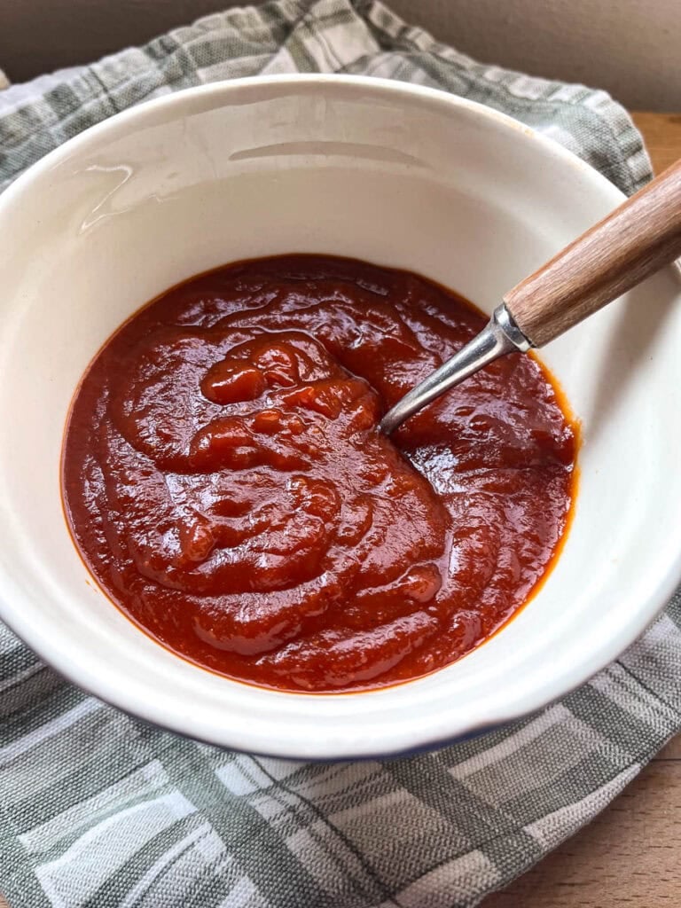 Homemade barbecue sauce in an ironstone bowl with a spoon.