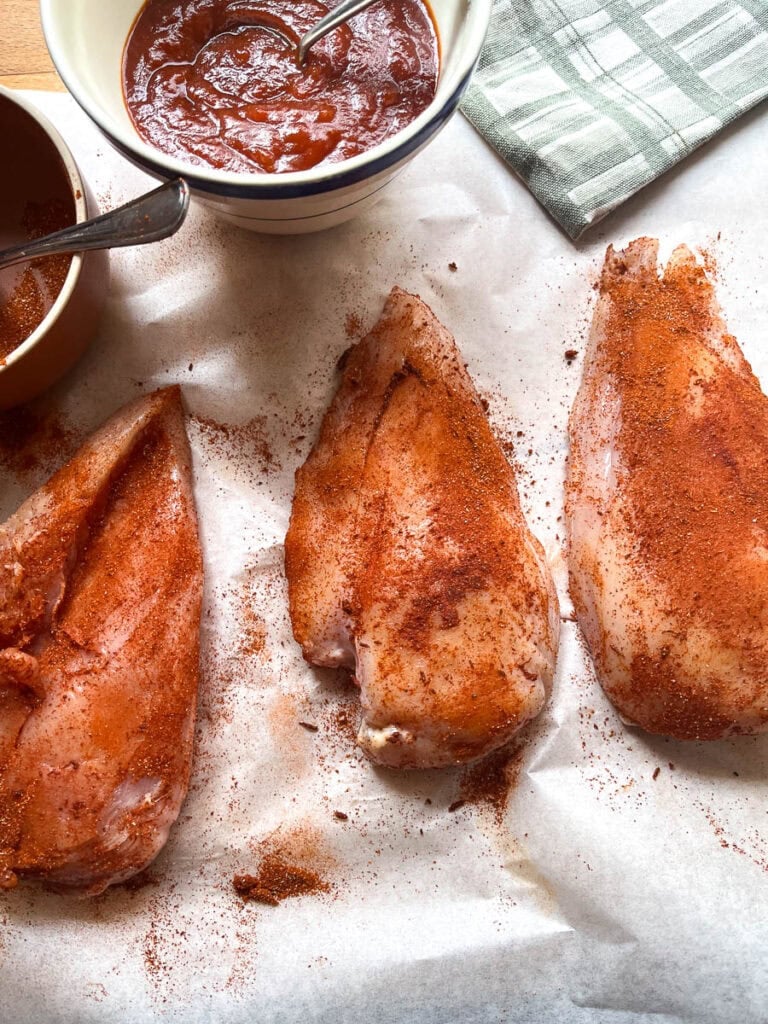 Three boneless chicken breasts rubbed with spices.