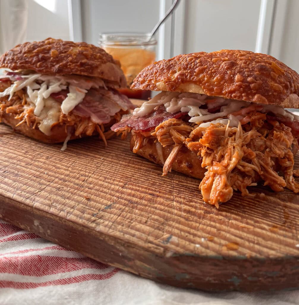 Two barbecue pulled chicken sandwiches on a cutting board.