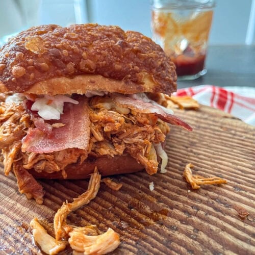 A loaded slow cooked pulled chicken sandwich on a wood cutting board.