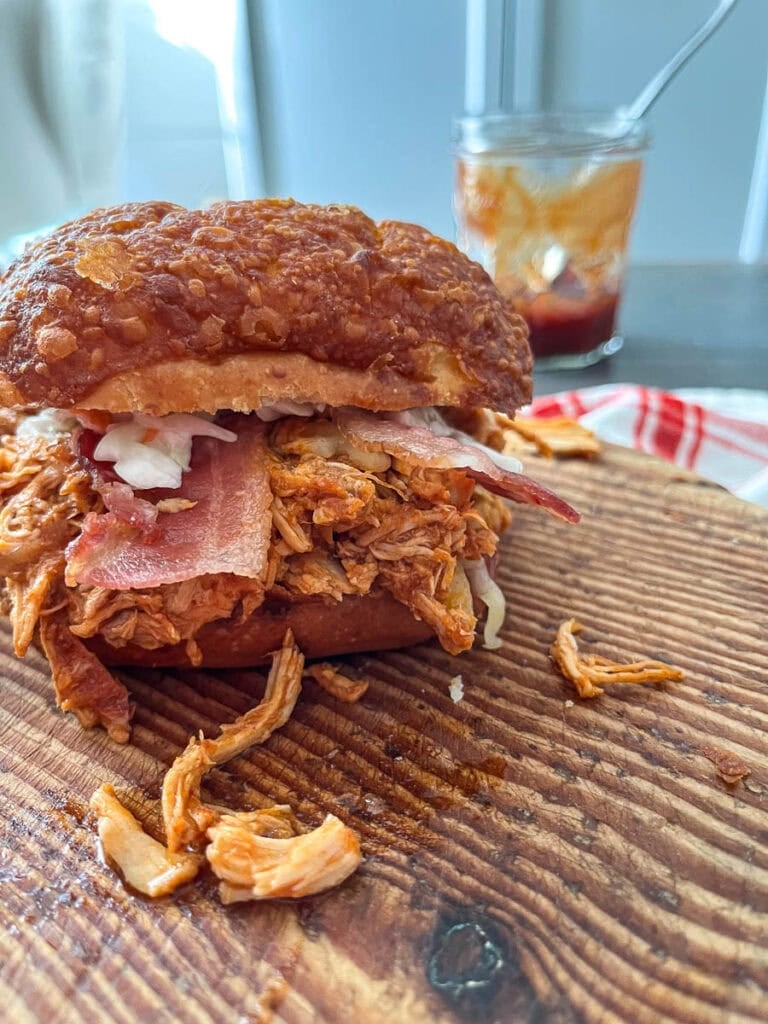 A loaded slow cooked pulled chicken sandwich on a wood cutting board.