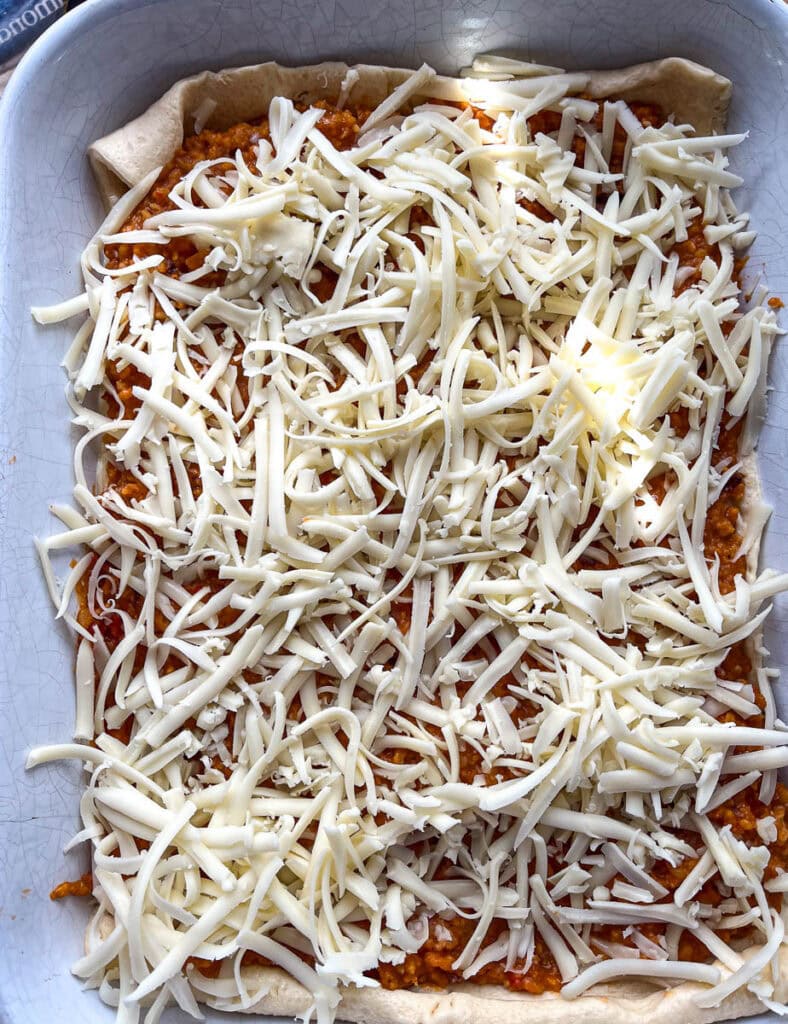 Freshly grated mozzarella cheese sprinkled over sloppy Joe filling in a casserole dish.