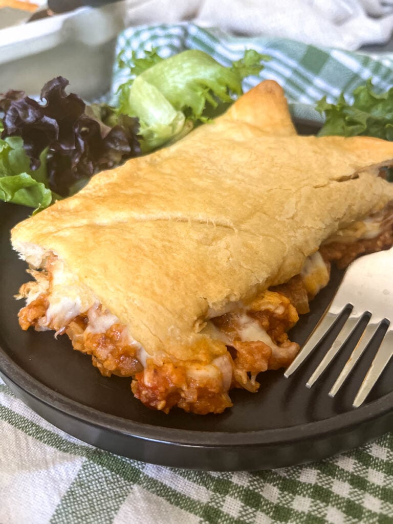 A slice of Sloppy Joe Crescent Rolls casserole with a side salad on a black dinner plate.