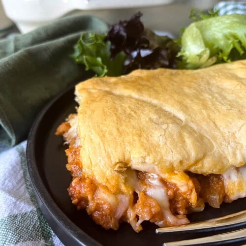 A slice of Sloppy Joe Crescent Rolls casserole with a side of salad on a black plate.