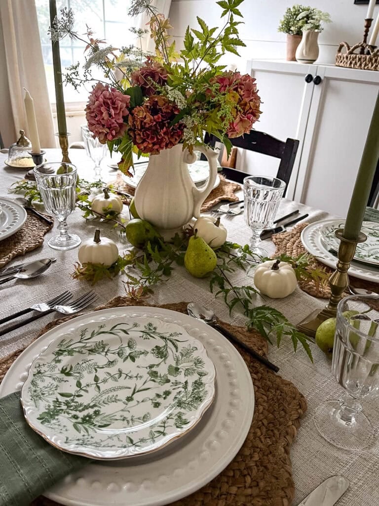 A charming fall tablescape set with green botanical salad plates on top of white dinner plates and a centrepiece of aging hydrangeas and Queen Anne's lace.