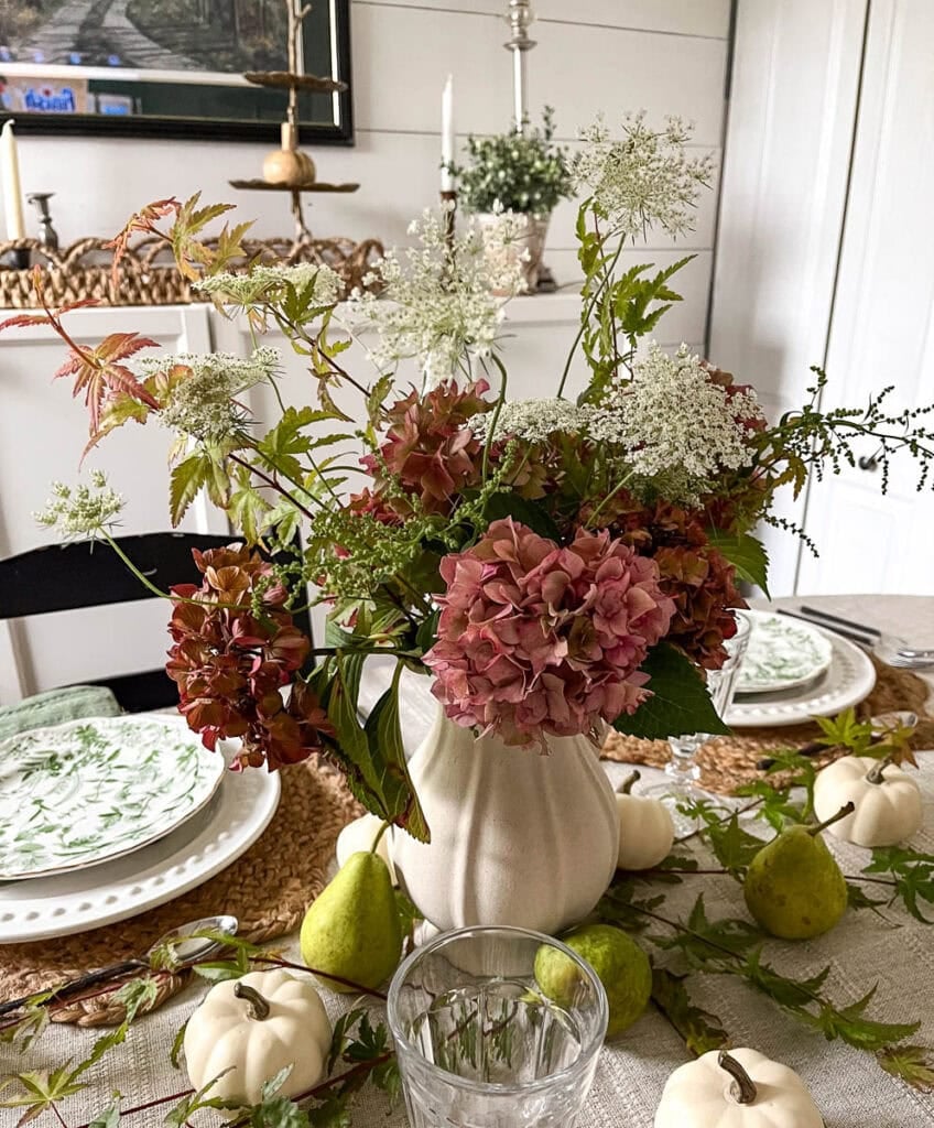 A rustic dinner table centrepiece made from aging hydrangeas in deep shades of pink, Queen Anne's lace and slim branches of Japanese red maple.