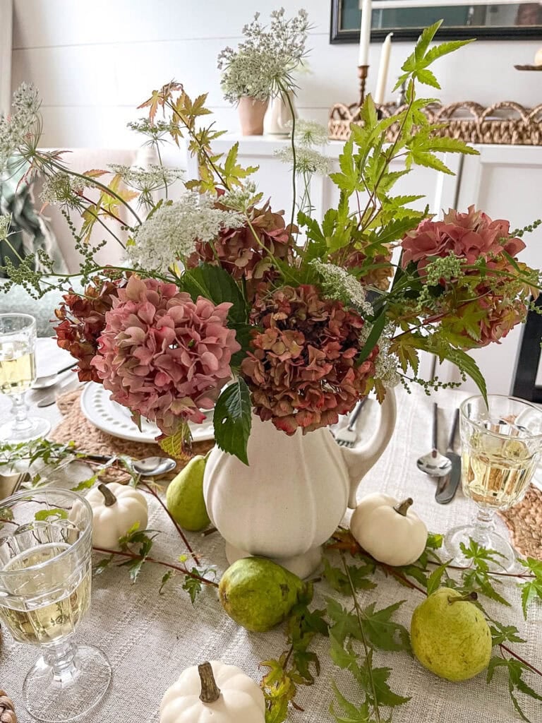 A rustic dinner table centrepiece made from aging hydrangeas in deep shades of pink, Queen Anne's lace and slim branches of Japanese red maple.