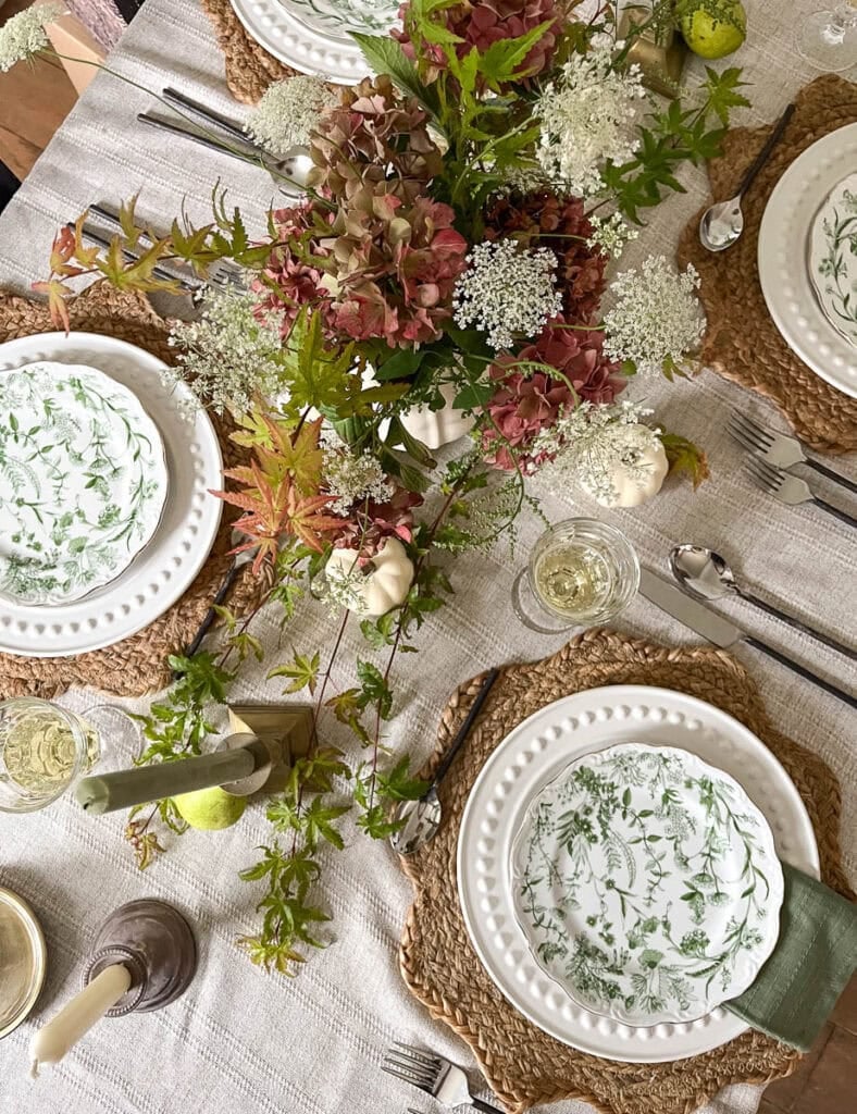 Overhead view of a table set for autumn with green botanical plates, garden flower centrepiece, fresh pears and faux mini white pumpkins.