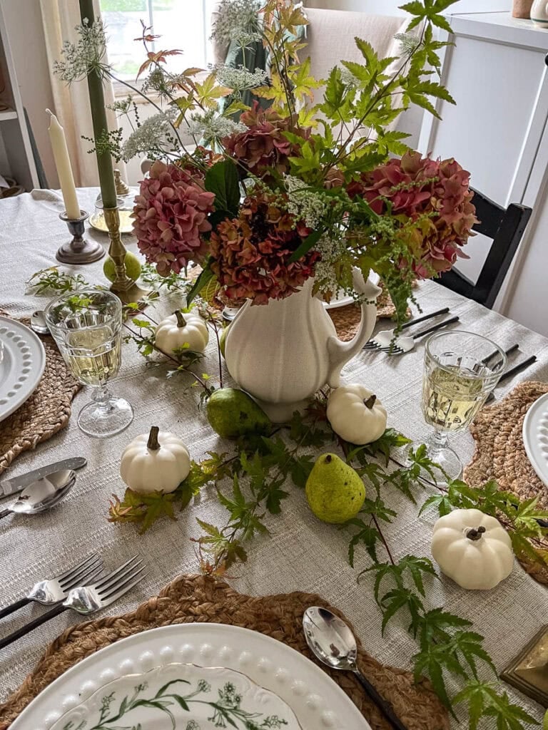 A rustic centrepiece of aging hydrangeas from the garden on a tablescape with creamy mini pumpkins and green pears for autumn.