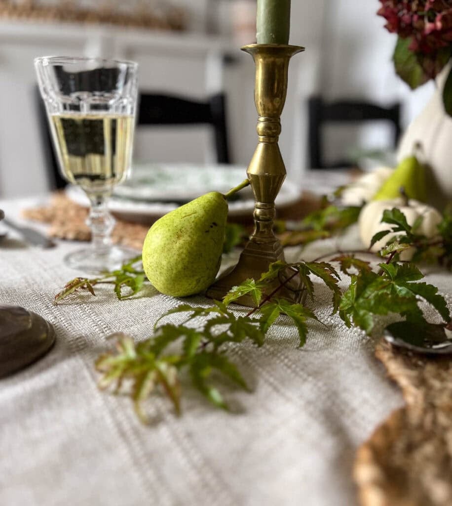 Japanese Maple branches, fresh green pears, brass candlesticks with green candles, and classic wine glasses with white wine on a table set for autumn.
