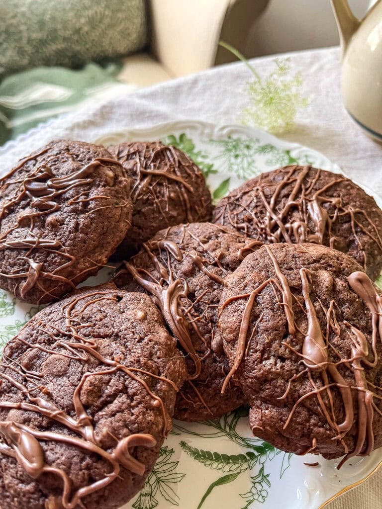 Six Chocolate Chip Brownie Cookies with a chocolate drizzle arranged on a green and white botanical print plate.