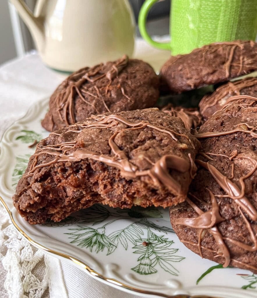 A plate of chocolate chip brownie cookies, one in the foreground with a bite out of it to show the inside.