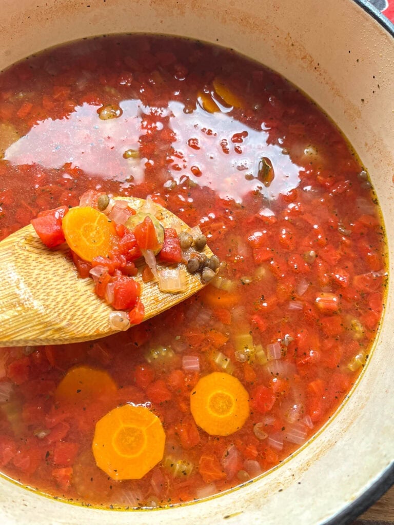 Cooked green lentils added to the tomato vegetable soup mixture in a dutch oven on the stove top.