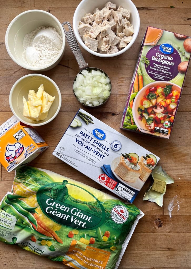 Ingredients to make chicken pot pie with puff pastry including cubed chicken, puff pastry shells, vegetable broth, butter and frozen mixed vegetables.