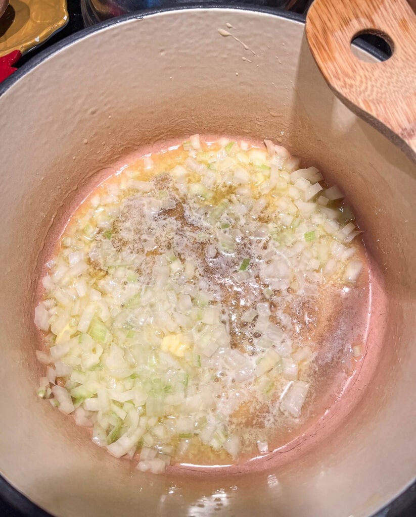 Chopped onions cooking in butter in a large dutch oven on the stove top.