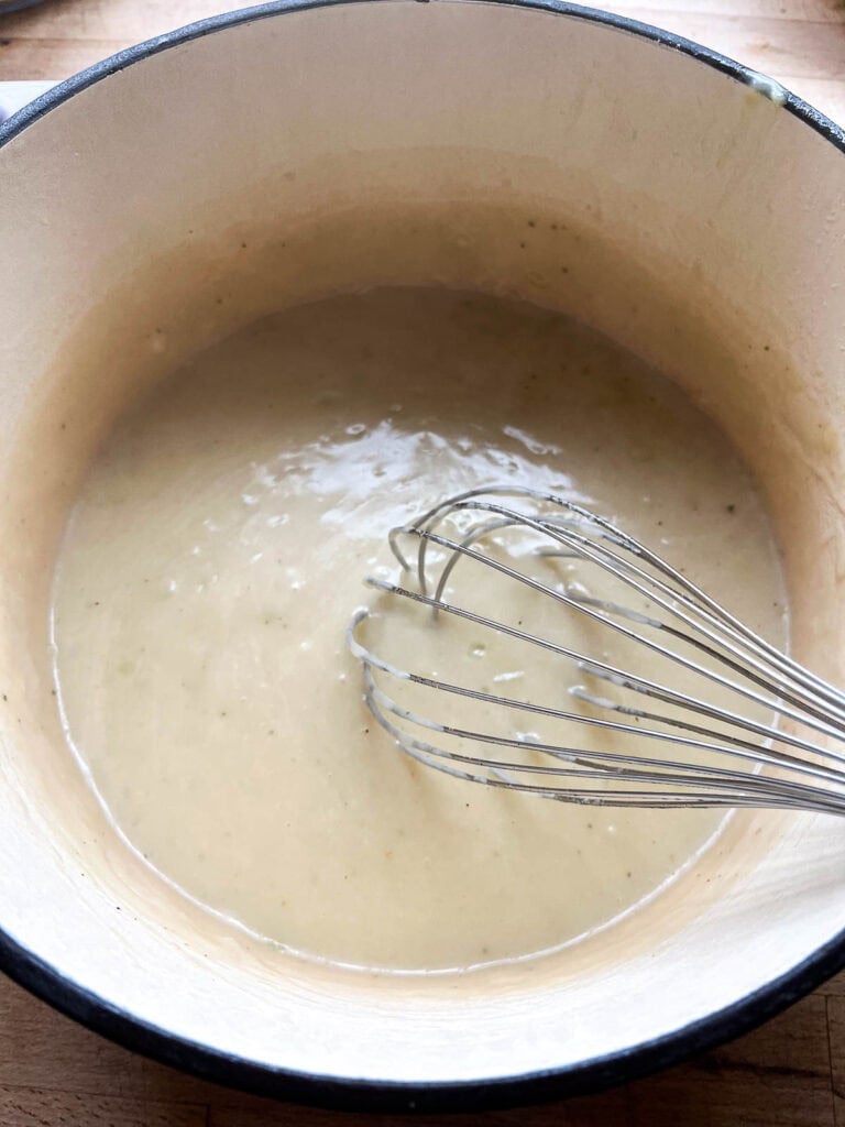 Broth added to the onion, butter and flour mixture, being stirred with a whisk to thicken.