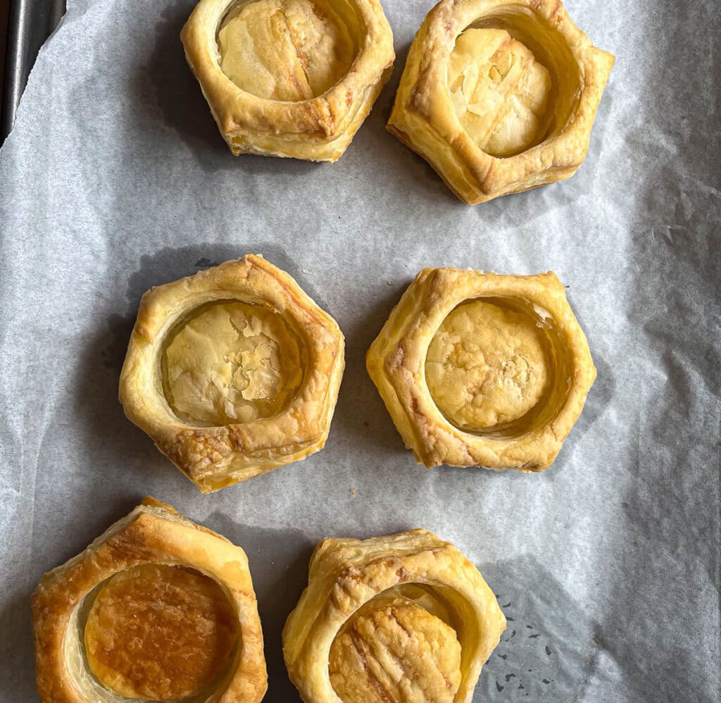 Freshly baked puff pastry shells on a parchment lined baking dish.