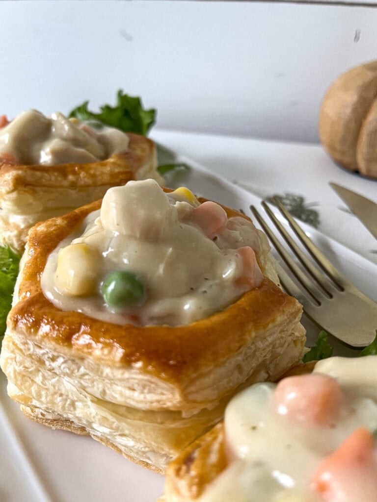 Chicken pot pie filling in puff pastry shells on a white patter.