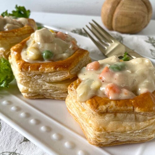 Three puff pastry shells filled with chicken pot pie filling on a long white platter.