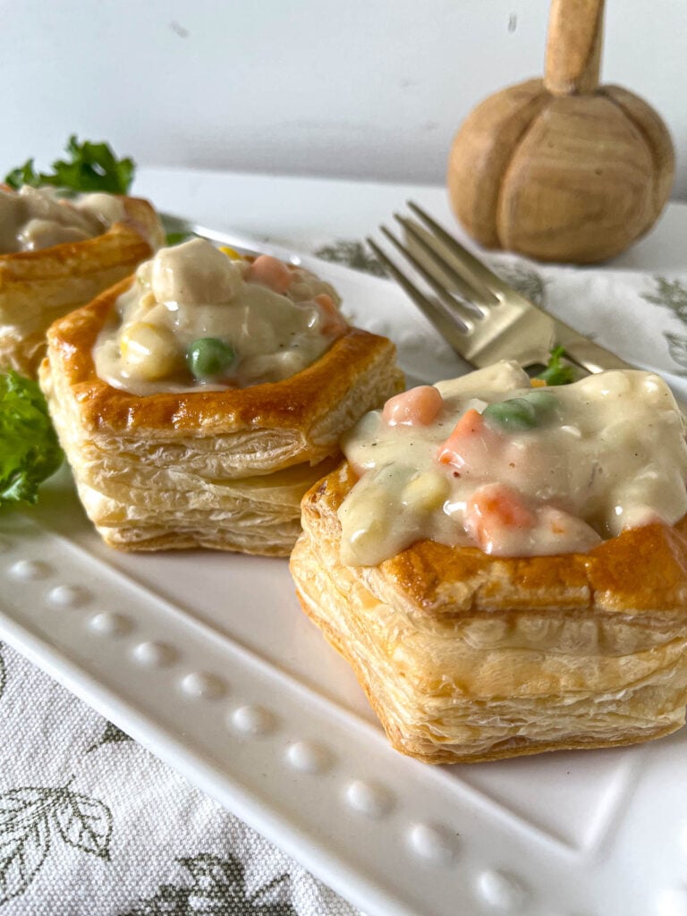 Three puff pastry shells filled with chicken pot pie filling on a long white platter.