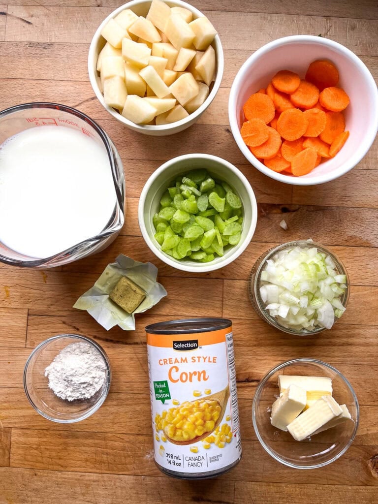 All the ingredients to make corn and potato chowder including canned creamed corn, cubed potatoes, sliced carrots, milk, chopped onion and chicken bouillon cube.