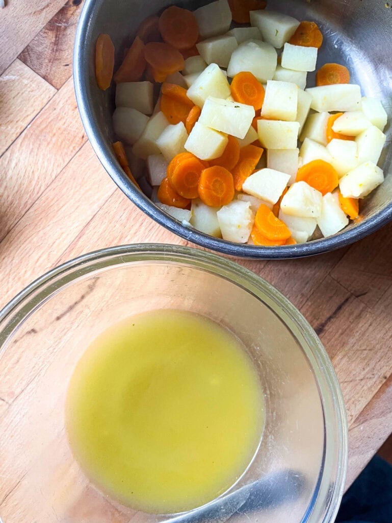 A pot of cooked potatoes and carrots in a saucepan with the cooking water that has been drained into a bowl to be used later.