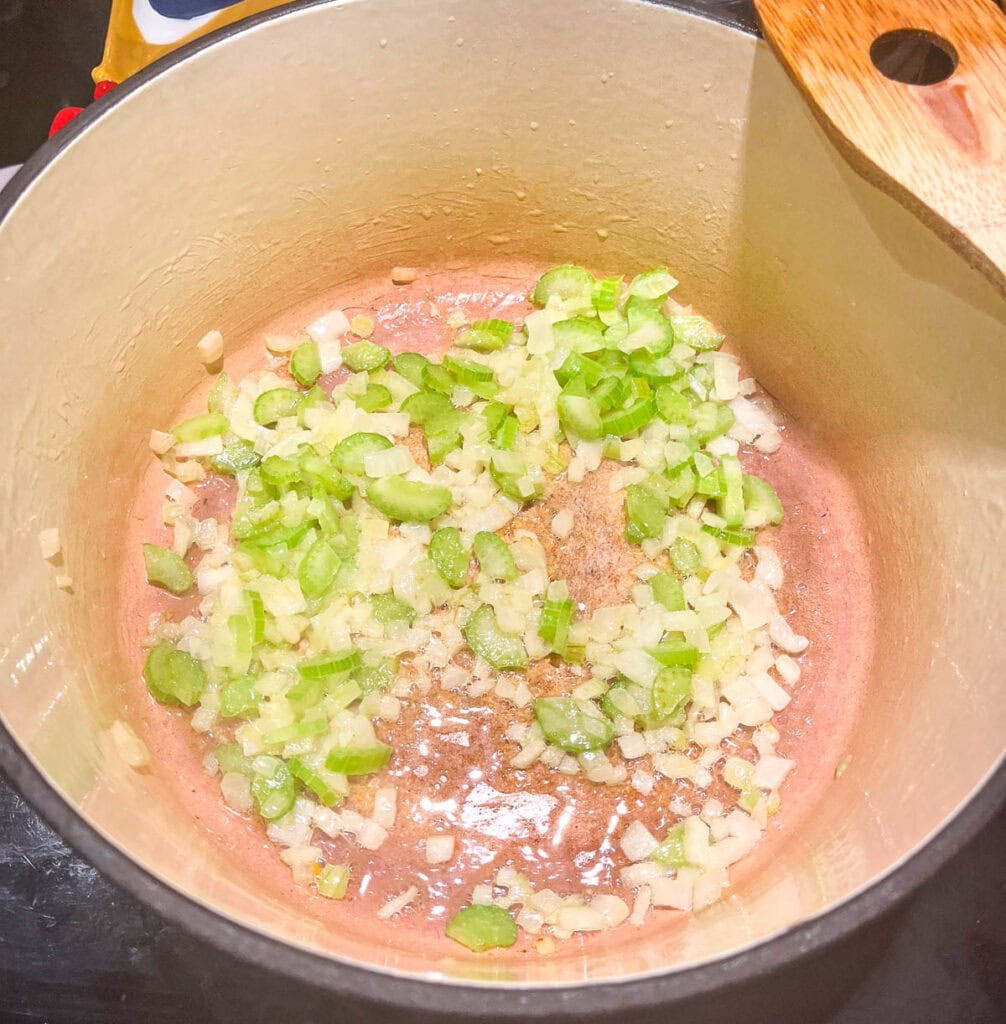 Chopped onions and celery cooking in melted butter in a dutch oven on the stove top.