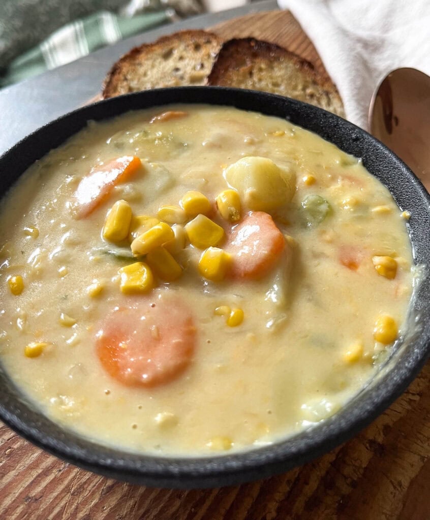 A bowl of corn and potato chowder a black bowl with 2 slices of toast on the side.
