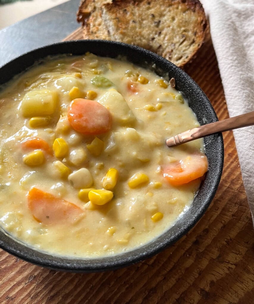 A bowl of potato corn chowder on a cutting board with a copper spoon in the bowl.