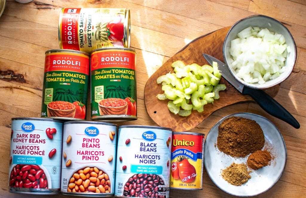 Ingredients to make 3 bean chili including canned diced tomatoes, kidney beans, pinto beans and black beans, chopped onion, celery and spices.