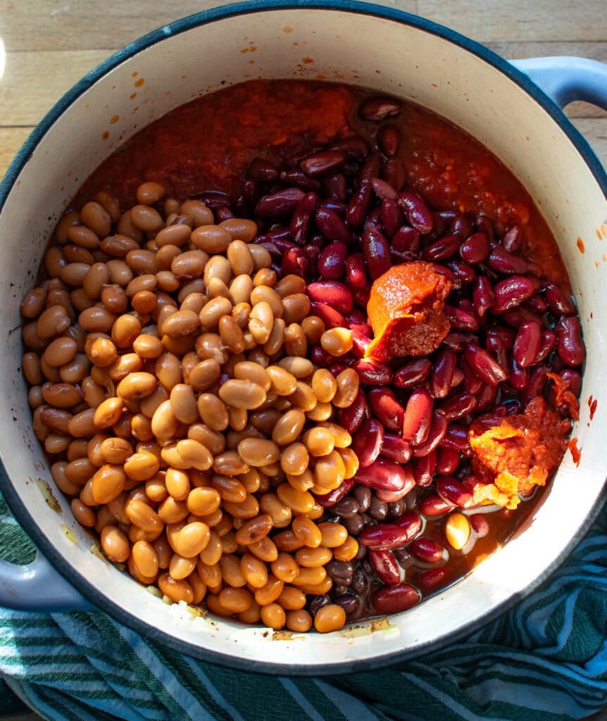 Beans, canned diced tomatoes, tomato sauce, and tomato paste added to the spiced onions and celery in a dutch oven.