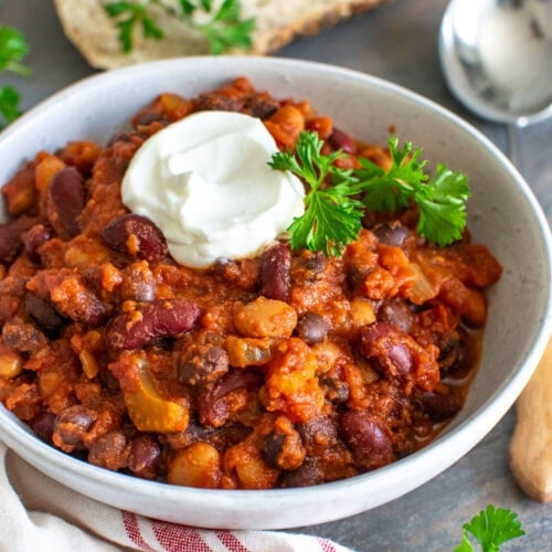 A bowl of 3 bean chili garnished with a dollop of sour cream and fresh parsley.