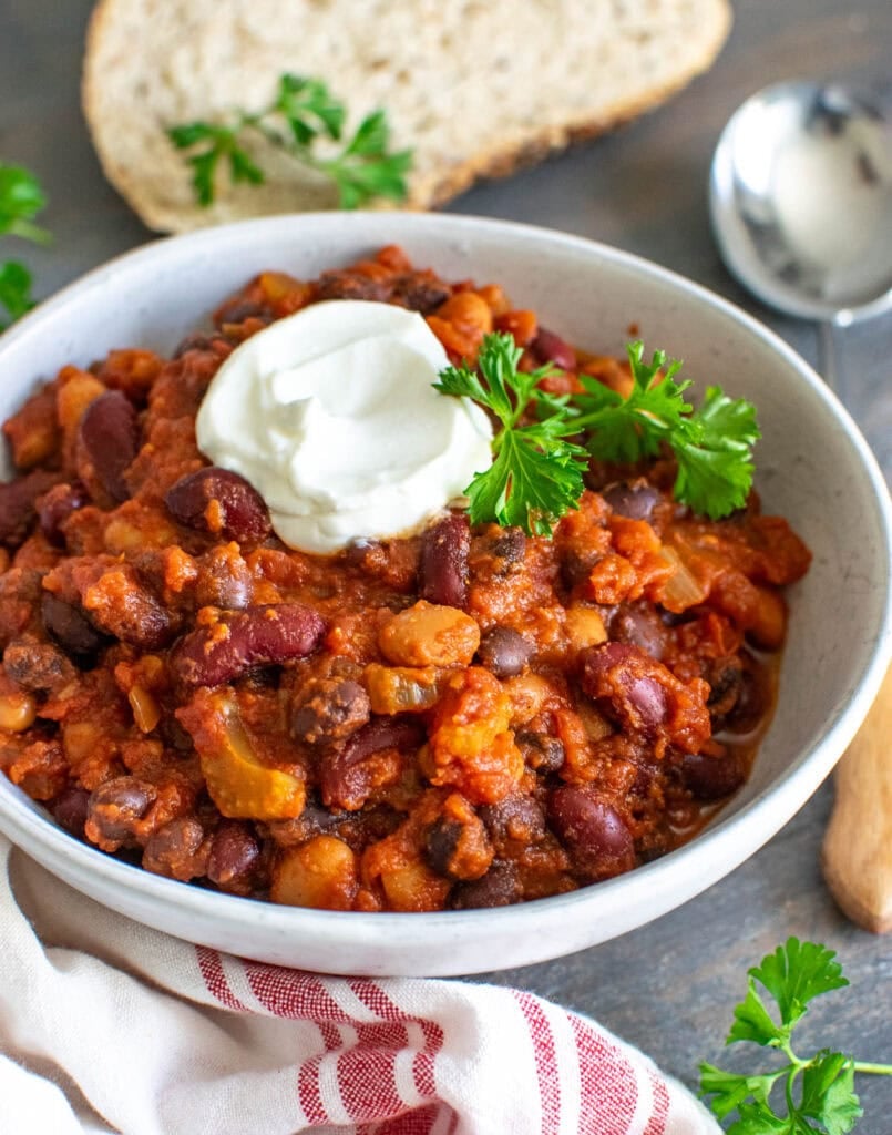 A bowl of 3 bean chili garnished with a dollop of sour cream and fresh parsley.