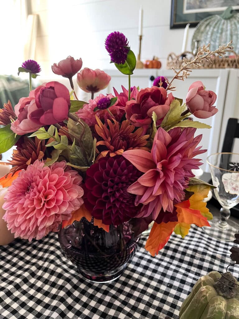 Dark and moody varieties of dahlias arranged in a dark purple vase as a centrepiece on a dining room table.