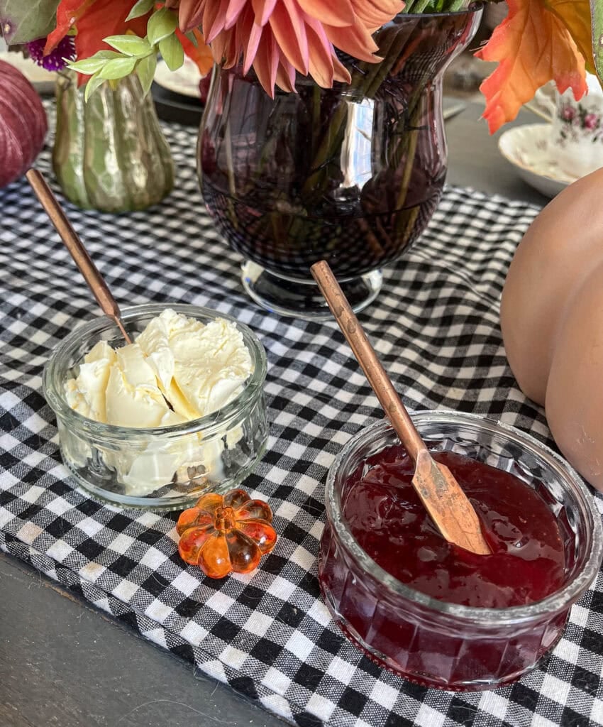 Clotted cream and strawberry jam in little glass bowls on a black and white check table runner.