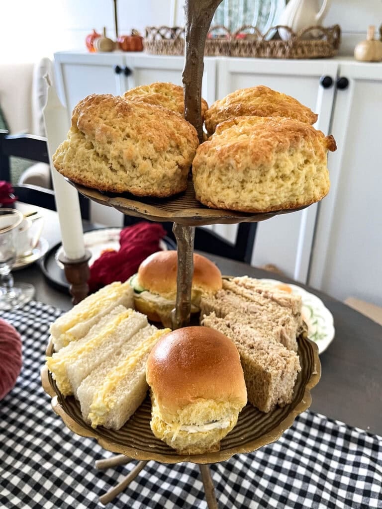 A 2-tiered stand with tea sandwiches on the bottom tier and scones on the top tier.