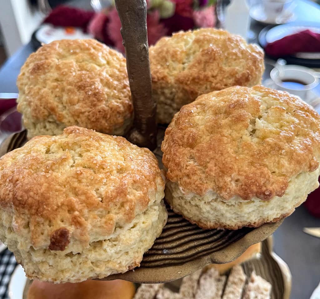 Four freshly made scones on the top tier of a two tiered plate.