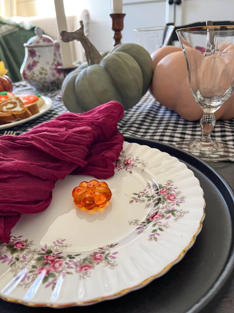 Two place settings for a Halloween Tea Party set with fine china, faux orange and green pumpkins on a black and white check table runner.
