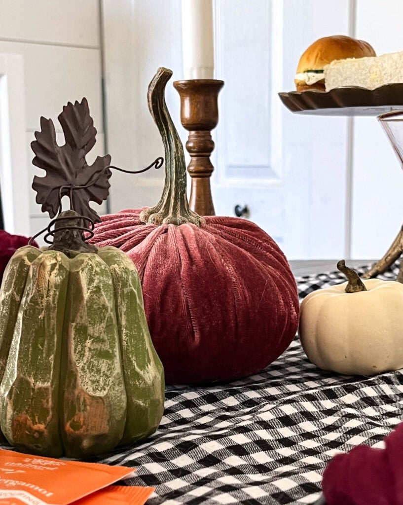 Three pumpkins on a Halloween tablescape. One burgundy velvet, one tiny white pumpkin and one an elongated green pumpkin with a metal leaf and stem.