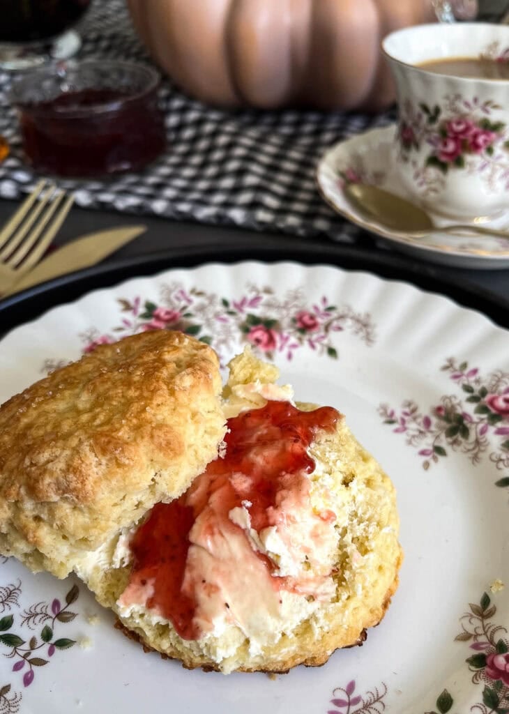 A scone dressed with clotted cream and strawberry jam on a Royal Albert lunch plate in the pattern Lavender Rose.